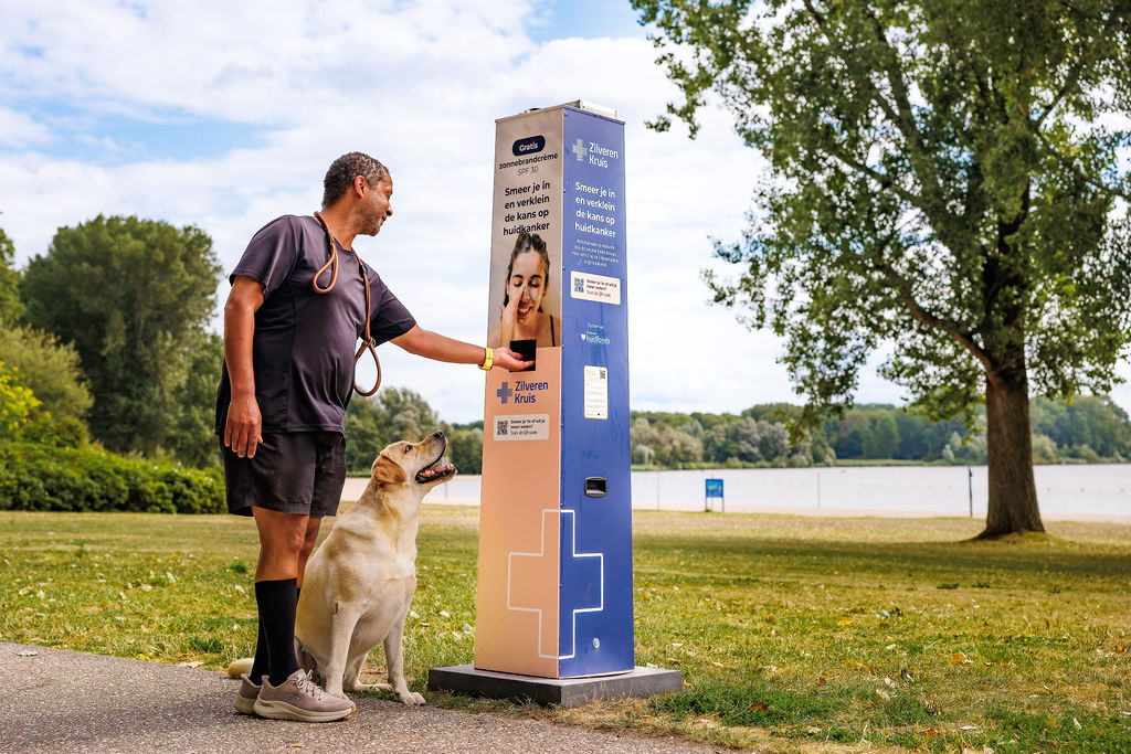 A man with a dog at a sunscreen station set up by the Dutch health insurance company Zilveren Kruis in a park by the lake