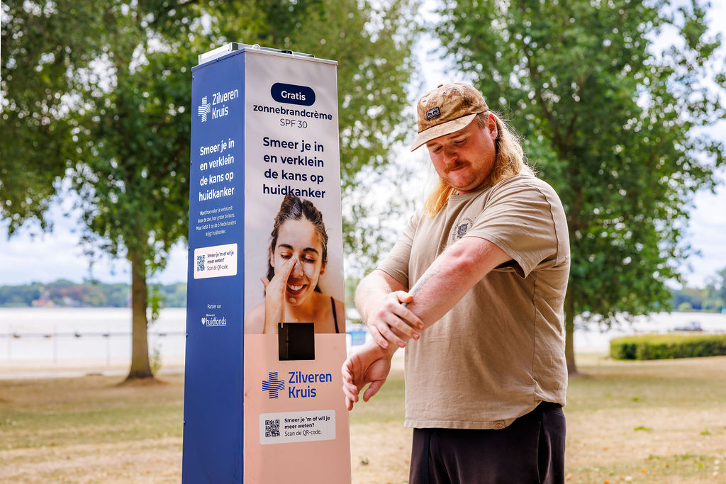 Mann cremt sich an einer Sonnencreme-Station der Krankenkasse Zilveren Kruis mit kostenloser Sonnencreme (LSF 30) am Wasser ein